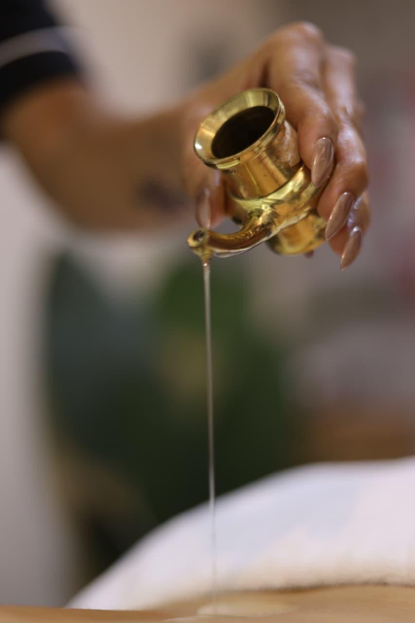 Warm oil being poured from a brass kalash for a massage ritual